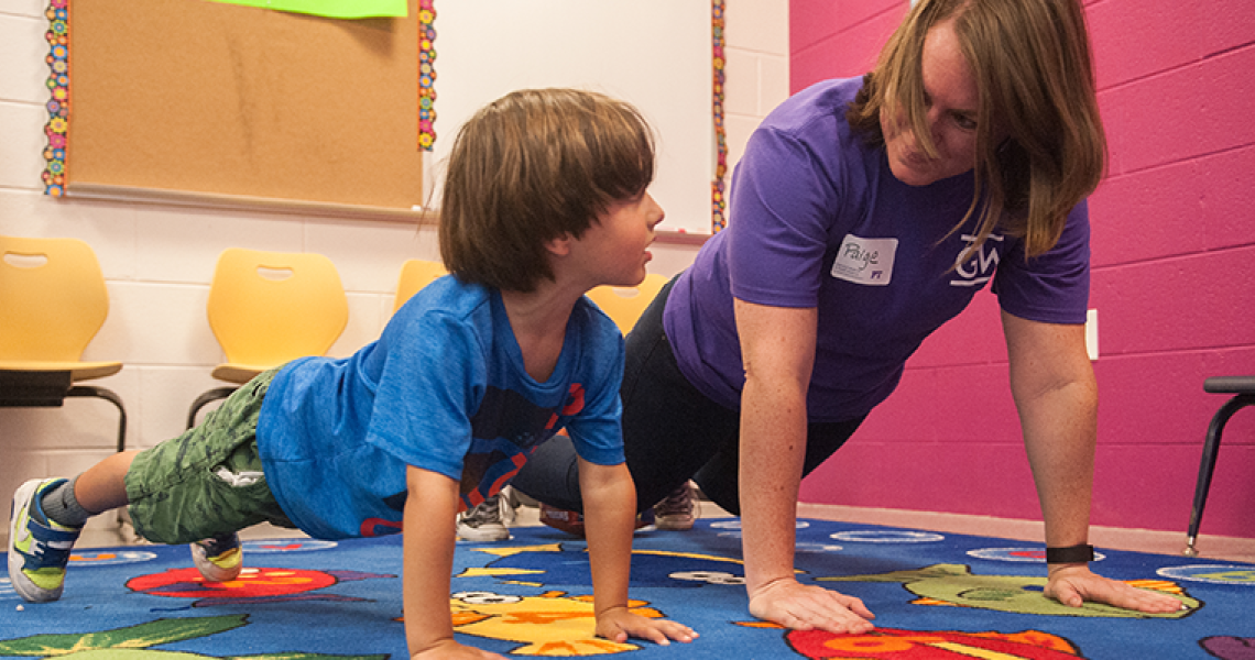 Child and physical therapist doing a push up together in a PT clinic