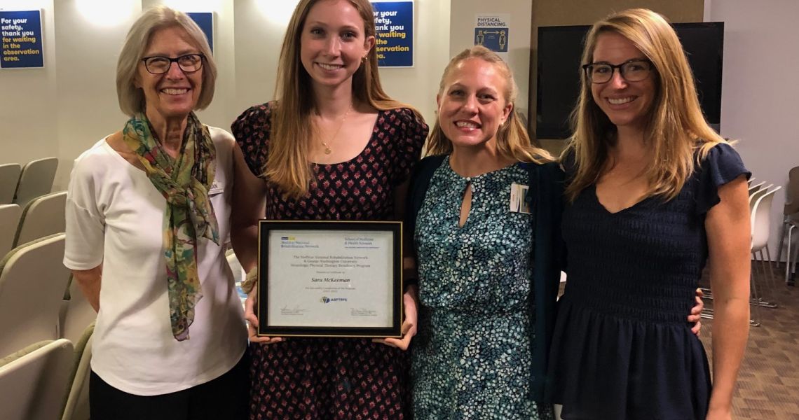 Resident stands holding her diploma with three mentors of the residency program