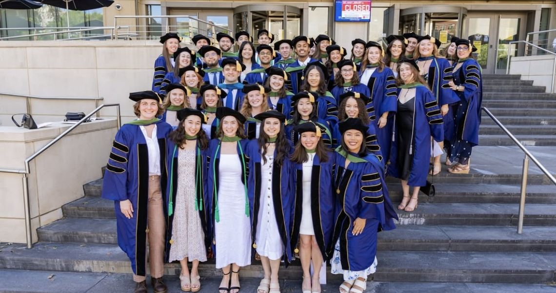 Class of 2025 dressed in graduation robes on steps of library