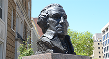 Bust of George Washington in front of green trees and campus buildings.