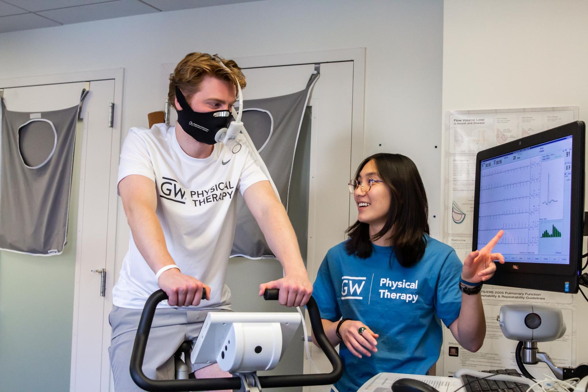 Student research assistant pointing to results of testing while participant performs bike exercise testing